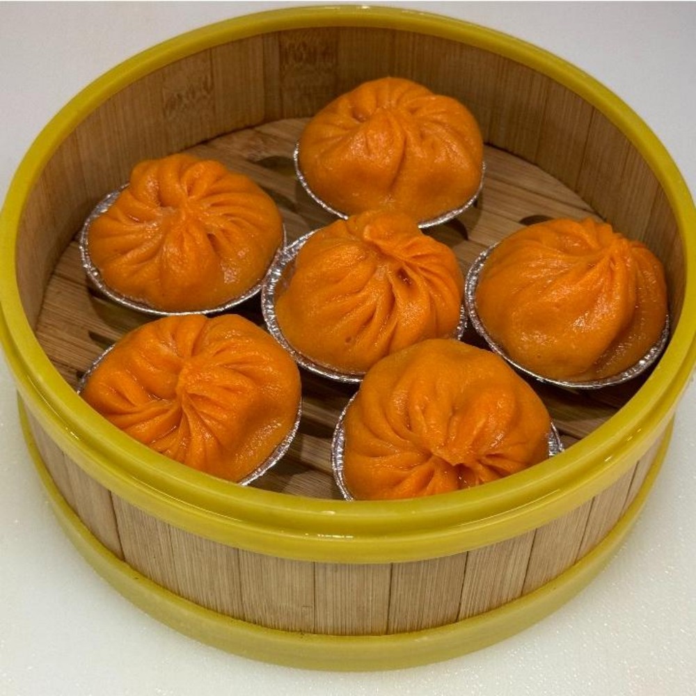 Six orange soup dumplings in bamboo steamer