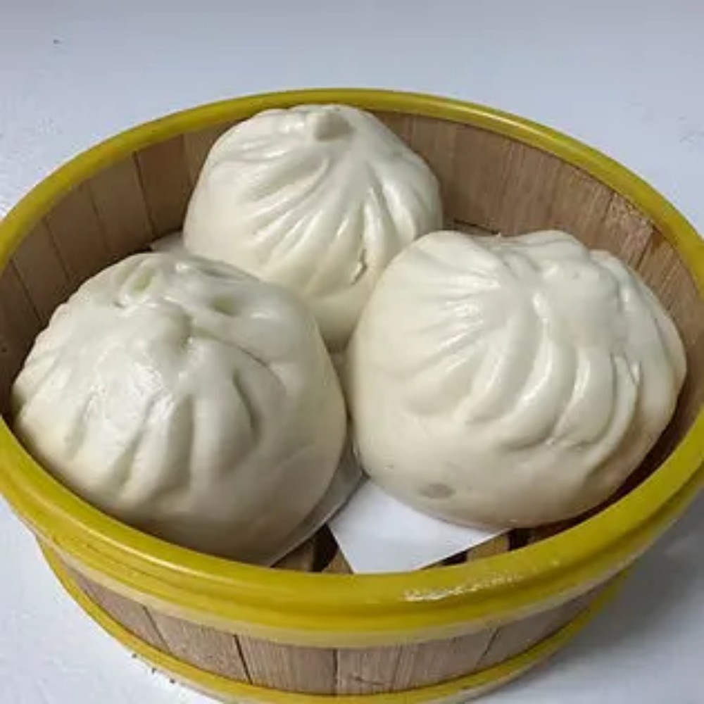 Three white steamed buns in bamboo steamer