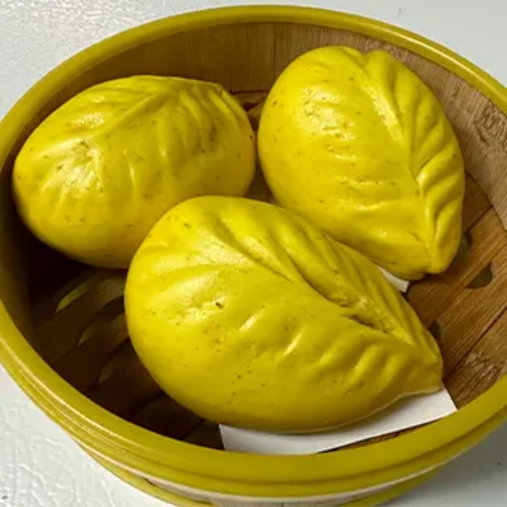 Three yellow leaf-shaped steamed buns in bamboo steamer