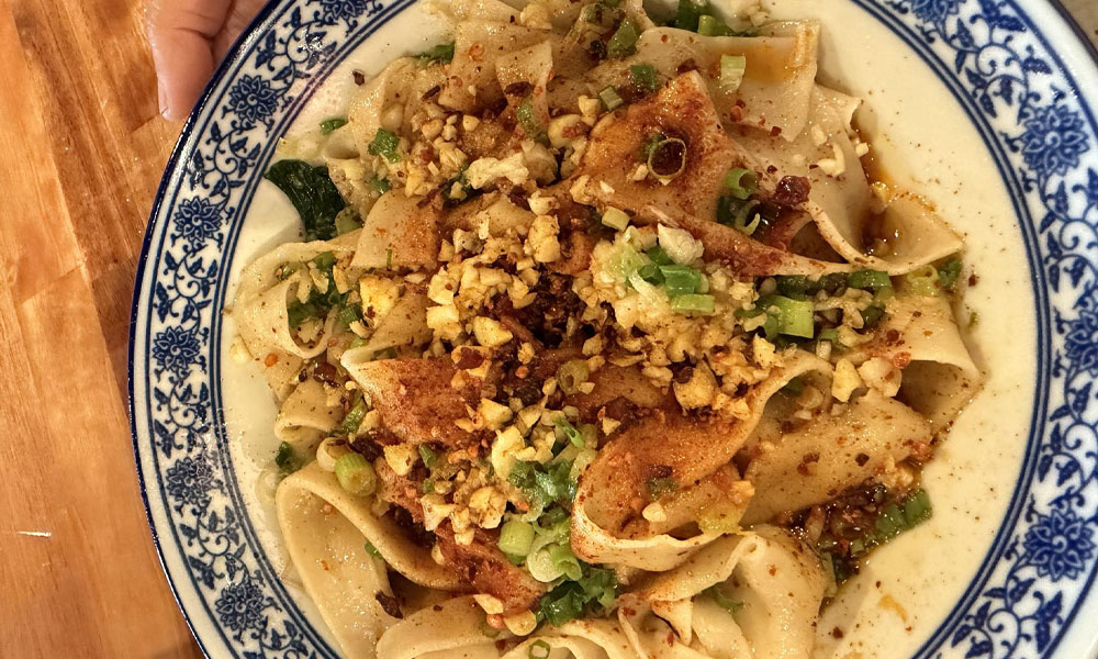 Dry spicy oil wide noodles topped with minced garlic, chili flakes and green scallions in blue floral ceramic bowl at Kung Fu Noodle House, a Chinese Restaurant in West Allis