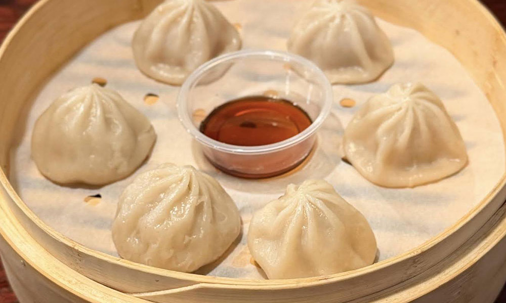 Steamed pork soup dumplings (xiaolongbao) in a bamboo steamer with soy sauce at Kungfu Noodles & Dumplings, a Chinese restaurant in College Station