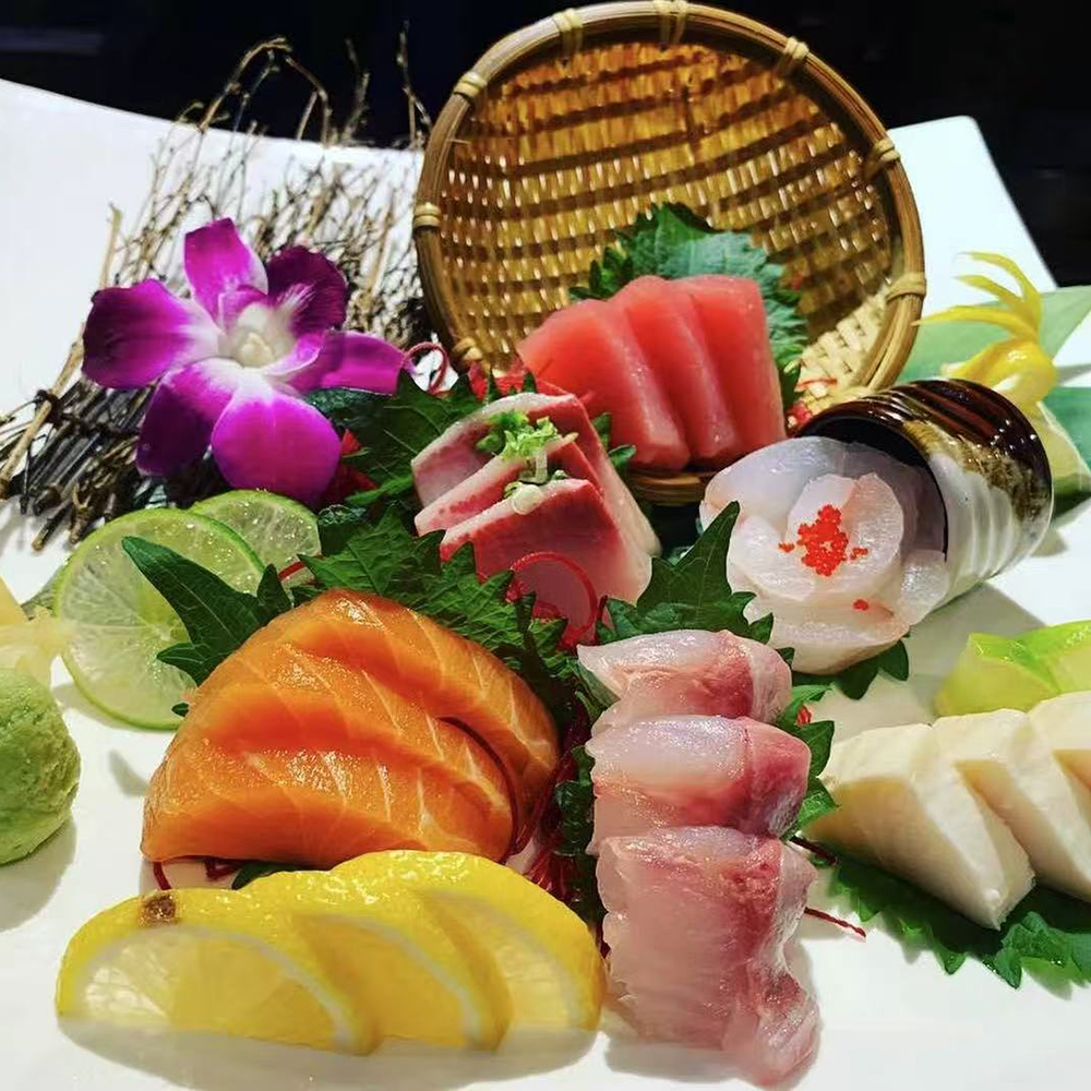 Lava-Buffet & Sushi-Asian-Fusion-Restaurant-assorted-sashimi-Kilgore A platter of assorted sashimi, featuring slices of salmon, tuna, and other fresh fish, garnished with lime wedges, a purple orchid, and green leaves, served with wasabi at Lava Buffet & Sushi,a Asian Fusion Restaurant in Kilgore