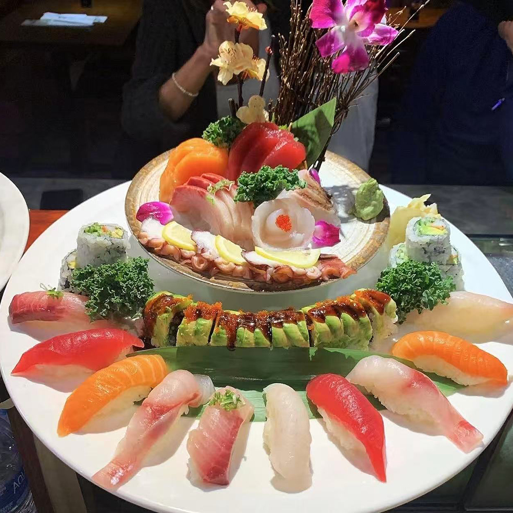 Lava-Buffet & Sushi-Asian-Fusion-Restaurant-assorted-sashimi-and-sushi-Kilgore A grand platter of assorted sushi and sashimi, with various nigiri, maki rolls, and sashimi pieces, decorated with flowers and greens, presented on a large white plate at Lava Buffet & Sushi,a Asian Fusion Restaurant in Kilgore