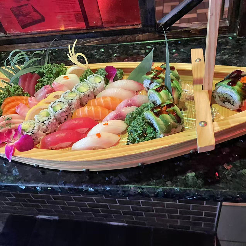 Lava-Buffet & Sushi-Asian-Fusion-Restaurant-Love-Boat-Kilgore A wooden boat - shaped platter filled with assorted sushi, including maki rolls and nigiri, garnished with flowers and greens, placed on a dark countertop at Lava Buffet & Sushi,a Asian Fusion Restaurant in Kilgore