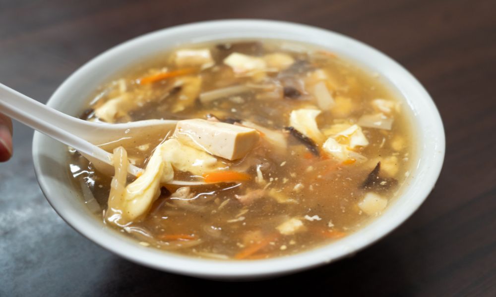 Hot and sour soup with tofu, mushrooms, and carrots in a white bowl at Legend Asian Fusion, a Asian fusion restaurant in Colonia