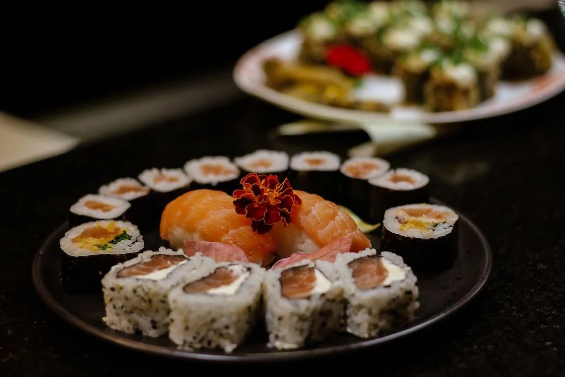 Black plate of assorted salmon sushi, including nigiri and rolls, with edible flower garnish at Legend Pot, Hot Pot Restaurant in Baton Rouge