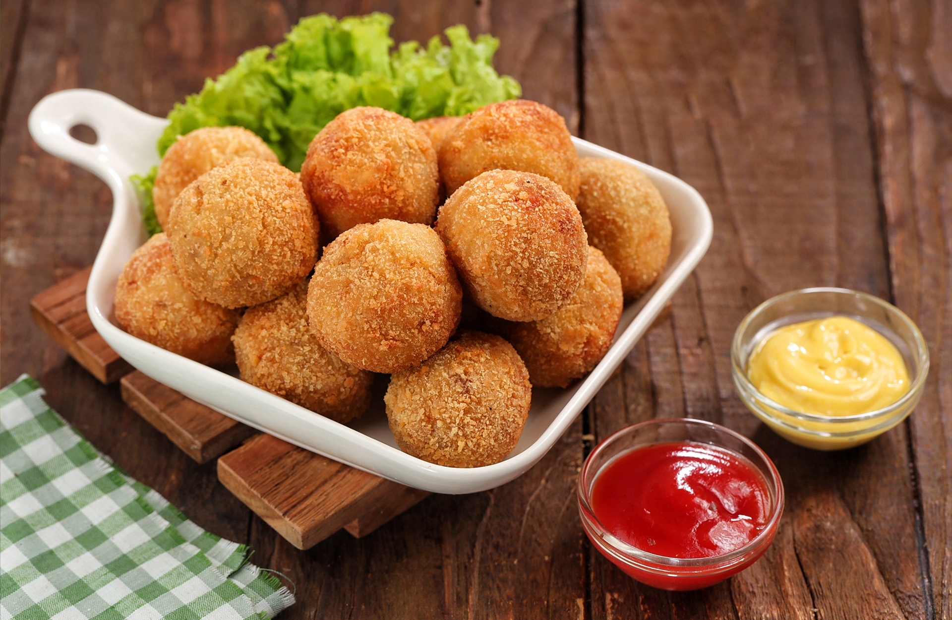 Golden fried food balls in a white dish with ketchup and mustard dips