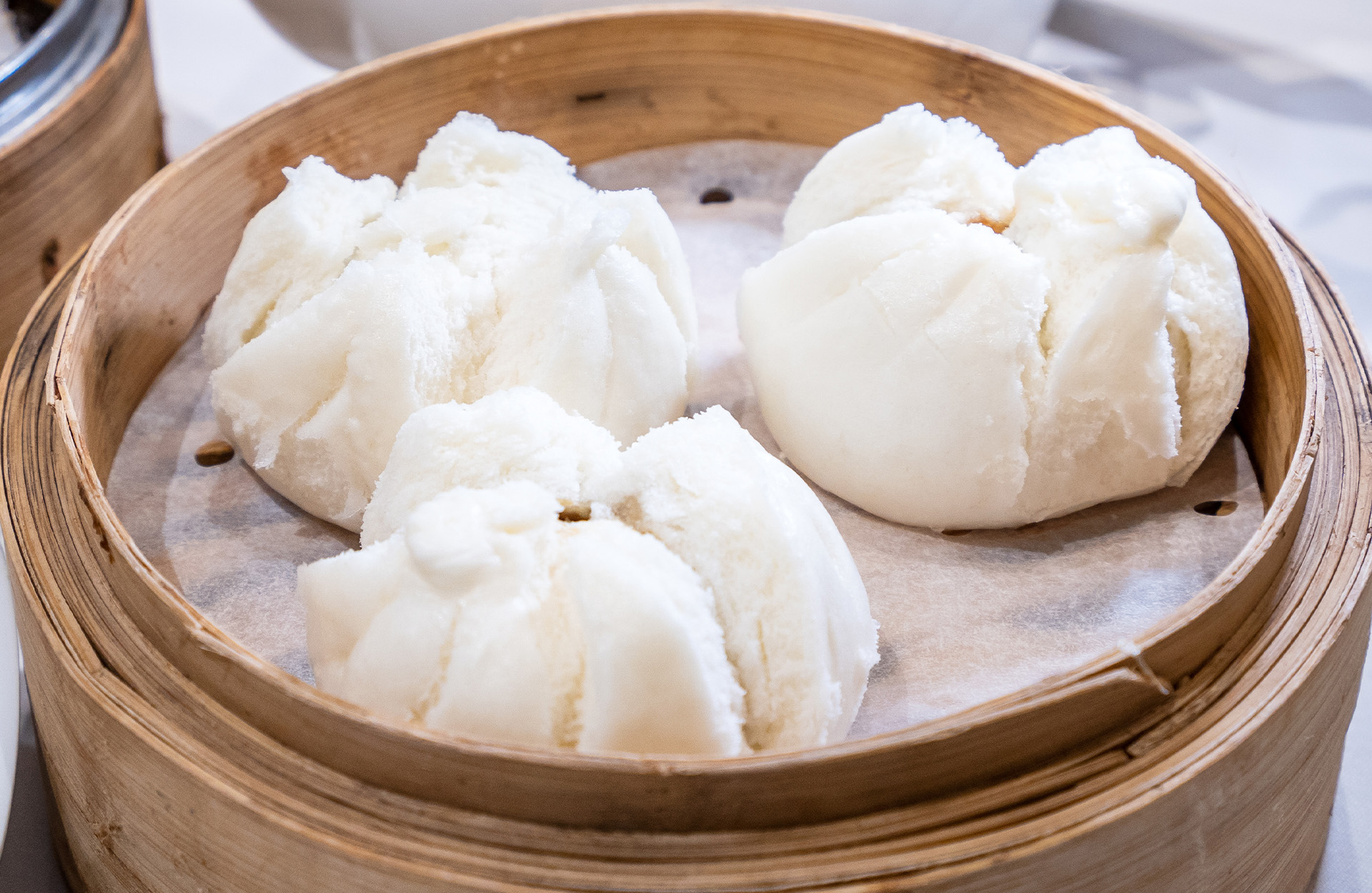Three fluffy white steamed buns sitting in a bamboo steamer