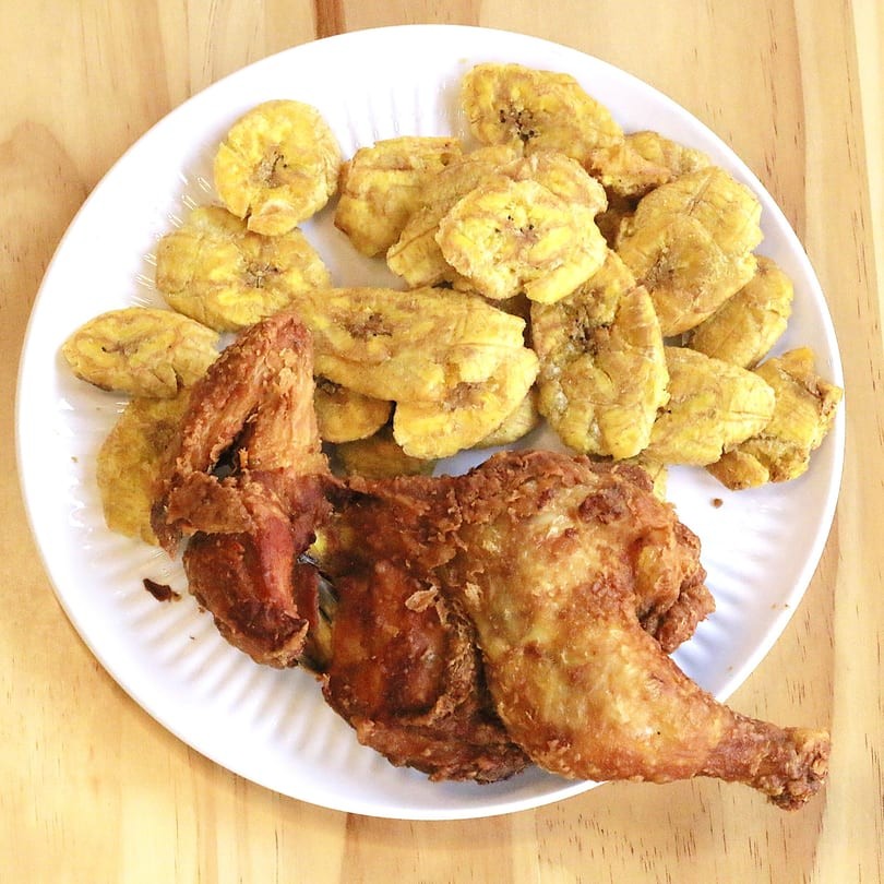 Fried chicken quarter and tostones on a white plate at Main Garden, a Chinese Fusion Restaurant in Passaic