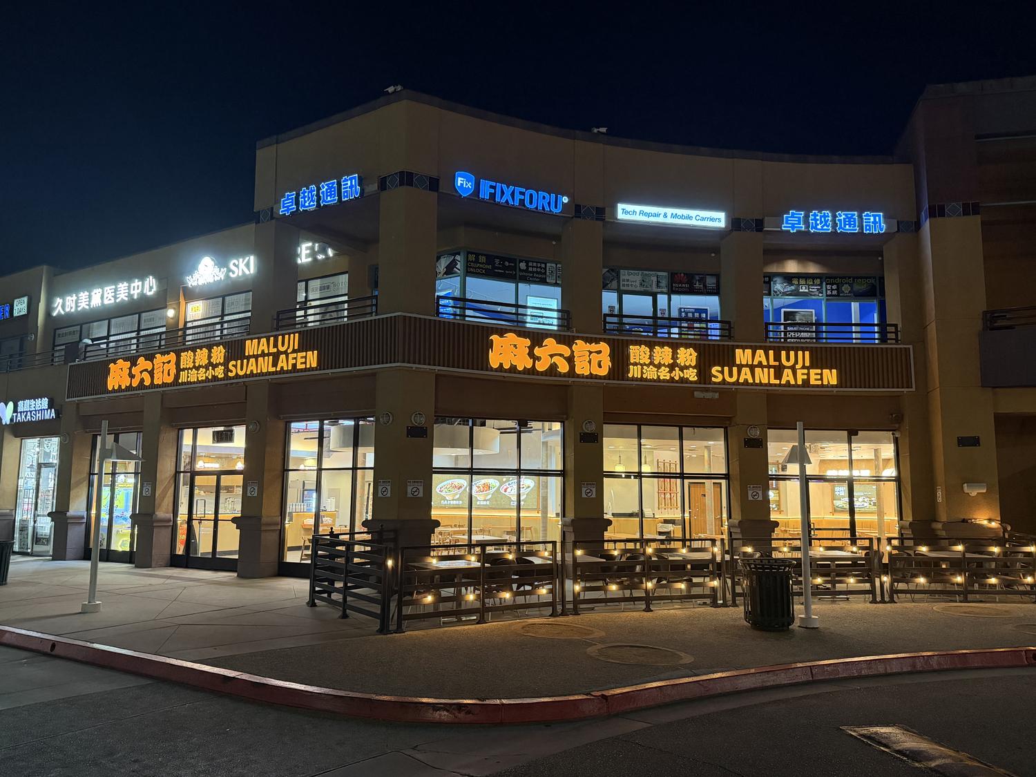 Night view of the brightly lit "Maluji Suanlafen" restaurant, featuring its glowing orange sign and cozy outdoor seating with string lights.