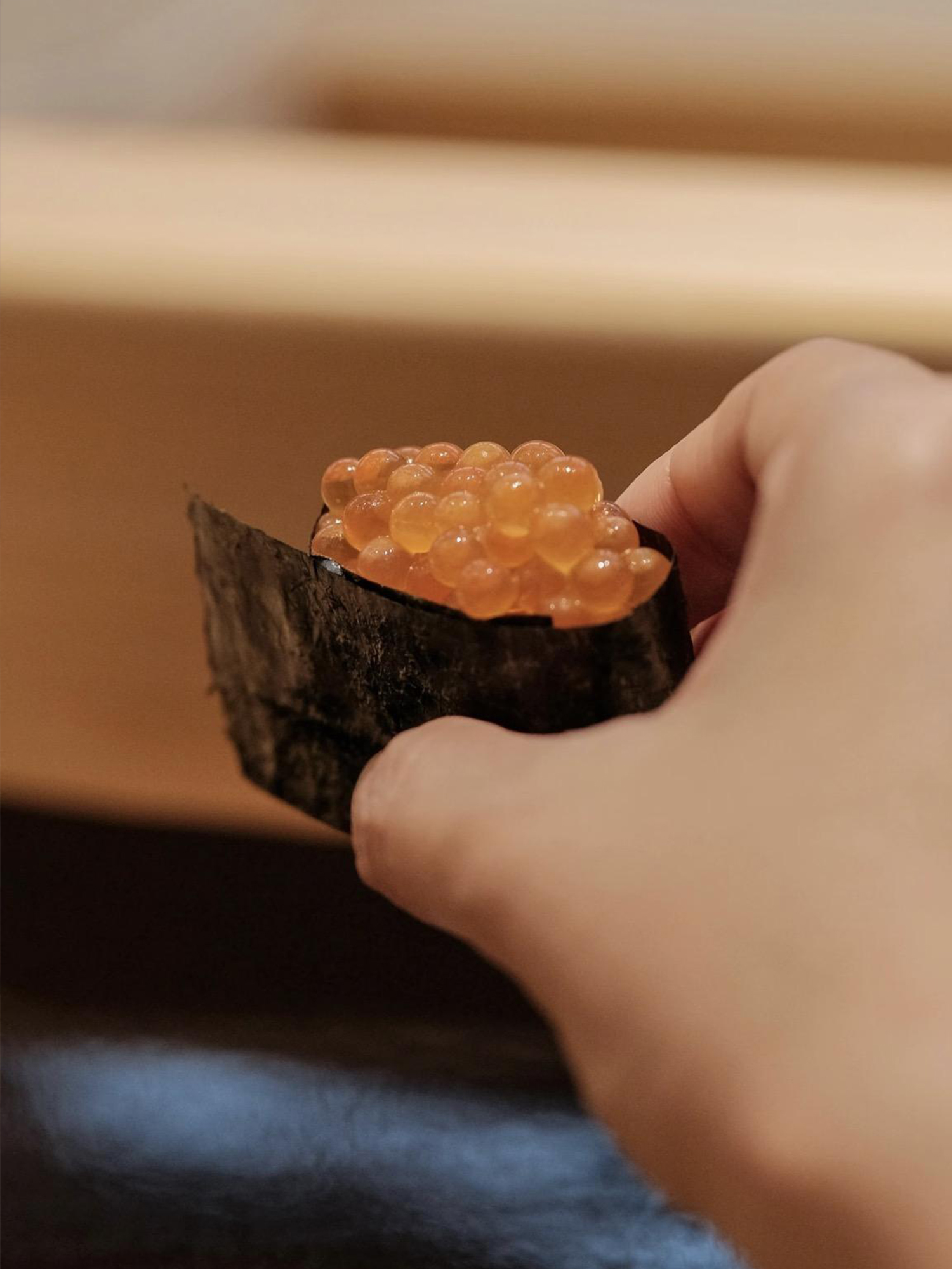 Hand holding a piece of salmon roe (ikura) gunkan sushi wrapped in seaweed.