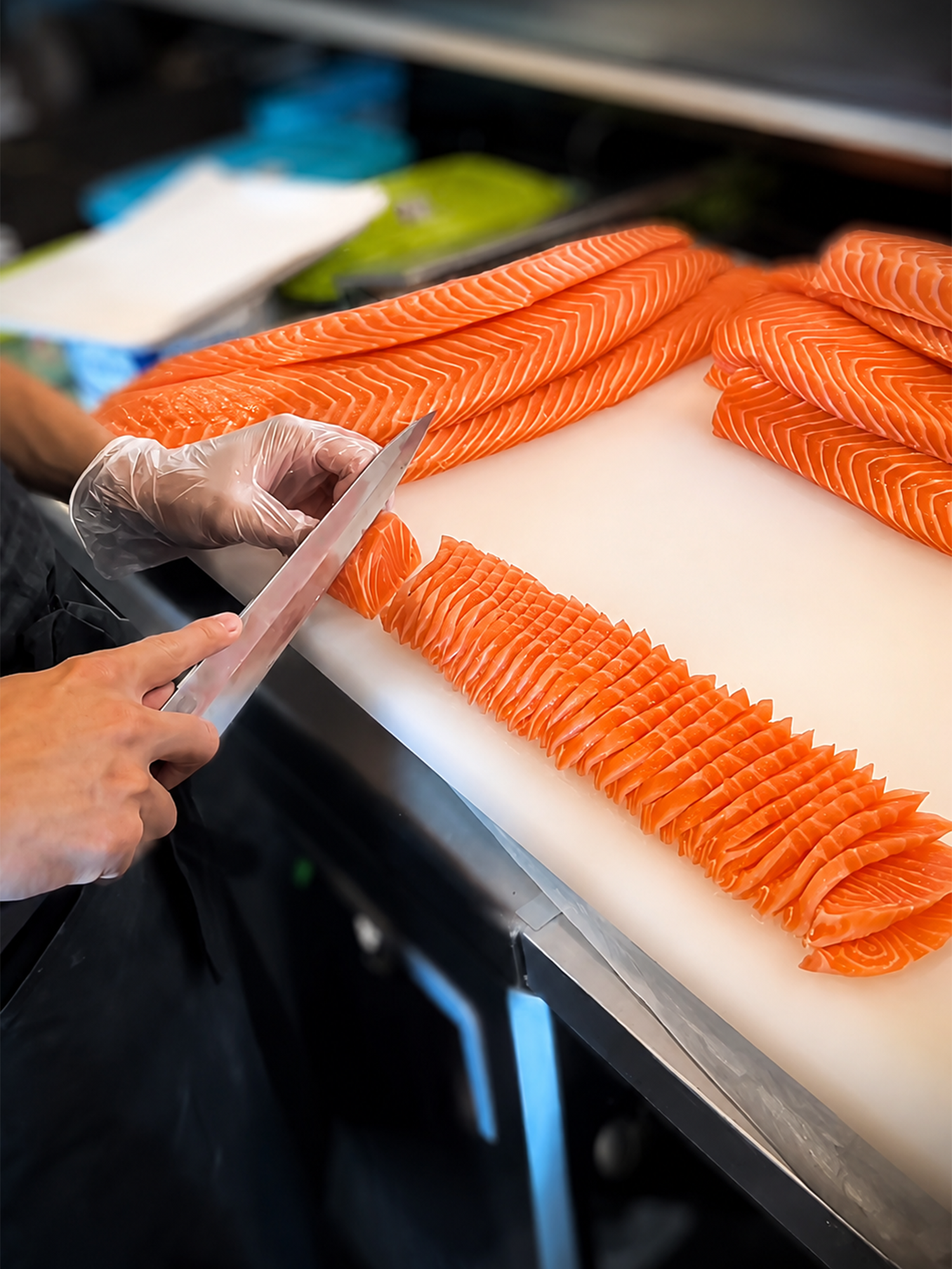 Sushi chef slicing fresh salmon fillets into thin pieces on a white cutting board.