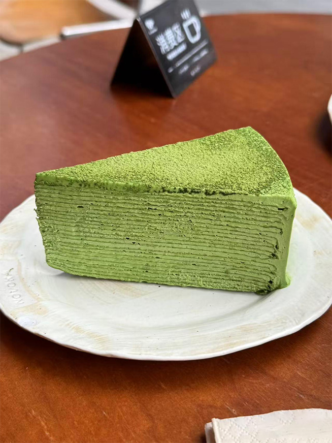 Slice of delicate layered matcha crepe cake set on off-white ceramic dining plate at Meet Again Cafe, a Cafe in Scotch Plains