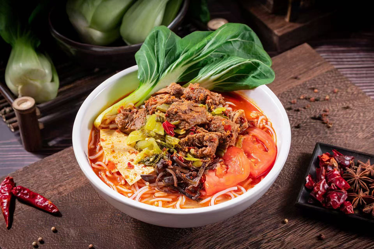 A bowl of braised beef rice noodles topped with chunks of beef, tomatoes, and vegetables at Meet Rice Noodle，a Authentic Rice Noodle Restaurant in Fremont