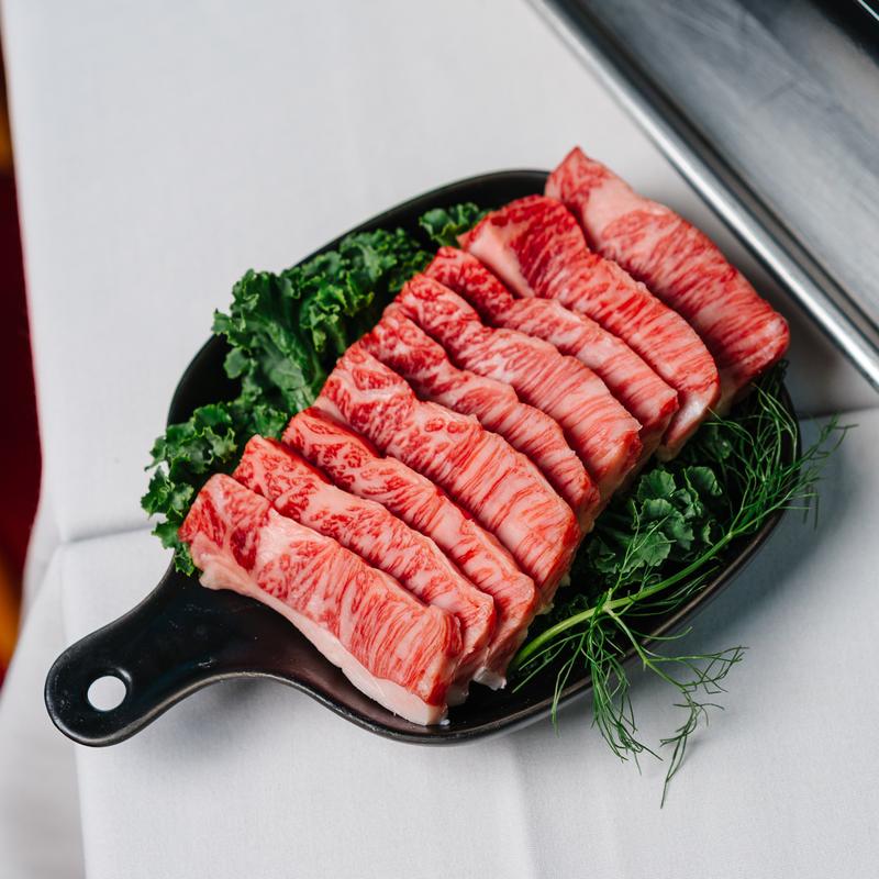 Platter of marbled premium beef slices with greens at Megu French Japanese Cuisine in Fort Worth