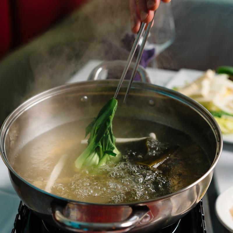 Cooking bok choy in shabu - shabu hot pot at Megu French Japanese Cuisine in Fort Worth