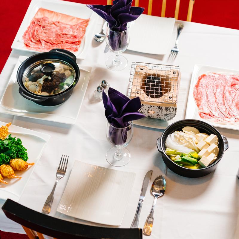 Table setting with various dishes including meat, clay pots and veggies at Megu French Japanese Cuisine in Fort Worth