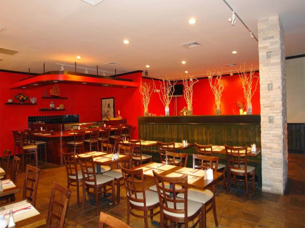 Warmly lit Japanese restaurant interior with red walls, wooden tables, a sushi bar, and decorative branches.