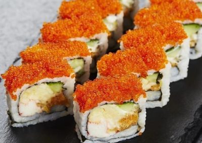 Fried seafood sushi roll covered in bright orange tobiko on a black slate platter at Mex Sushi Taco, a Asian restaurant in Place maspeth