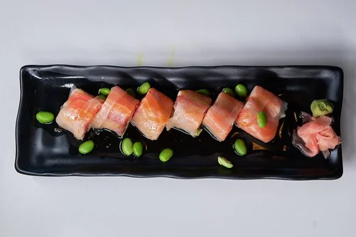 Mint-Bistro-Asian-Fusion-Restaurant-Salmon-Sashimi-with-Edamame-Milford Fresh salmon sashimi slices on a black plate, garnished with edamame at Mint Bistro,a Asian Fusion Restaurant in Milford