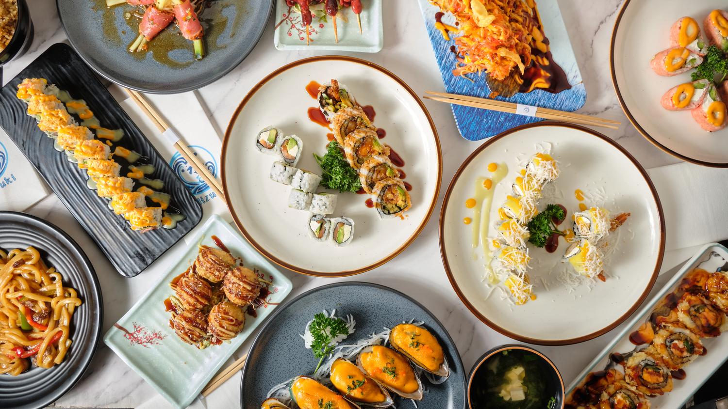 Top-down shot of assorted sushi rolls, mussels, udon and fried bites arranged on marble tableware at Mizuki sushi, a Japanese Restaurant in Baytown