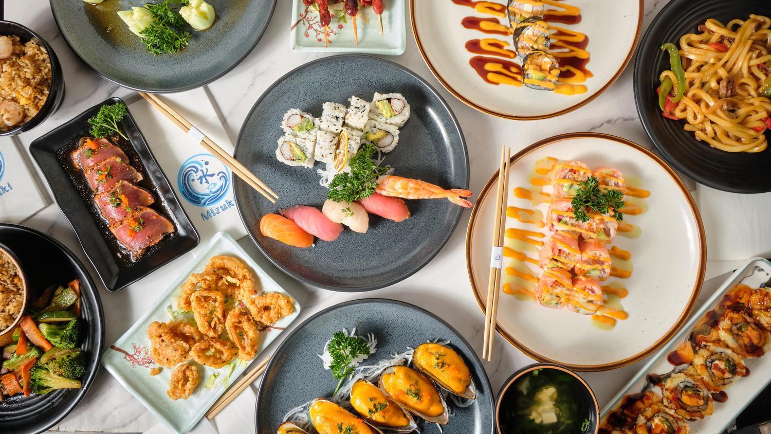 Overhead view of sashimi, sushi platters, tempura, fried rice and udon noodle dishes on marble counter at Mizuki sushi, a Japanese Restaurant in Baytown