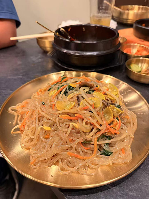Stir-fried glass noodles with vegetables on a golden plate at Mr.Kimchi Korean Bistro, a Korean Restaurant in Oklahoma City