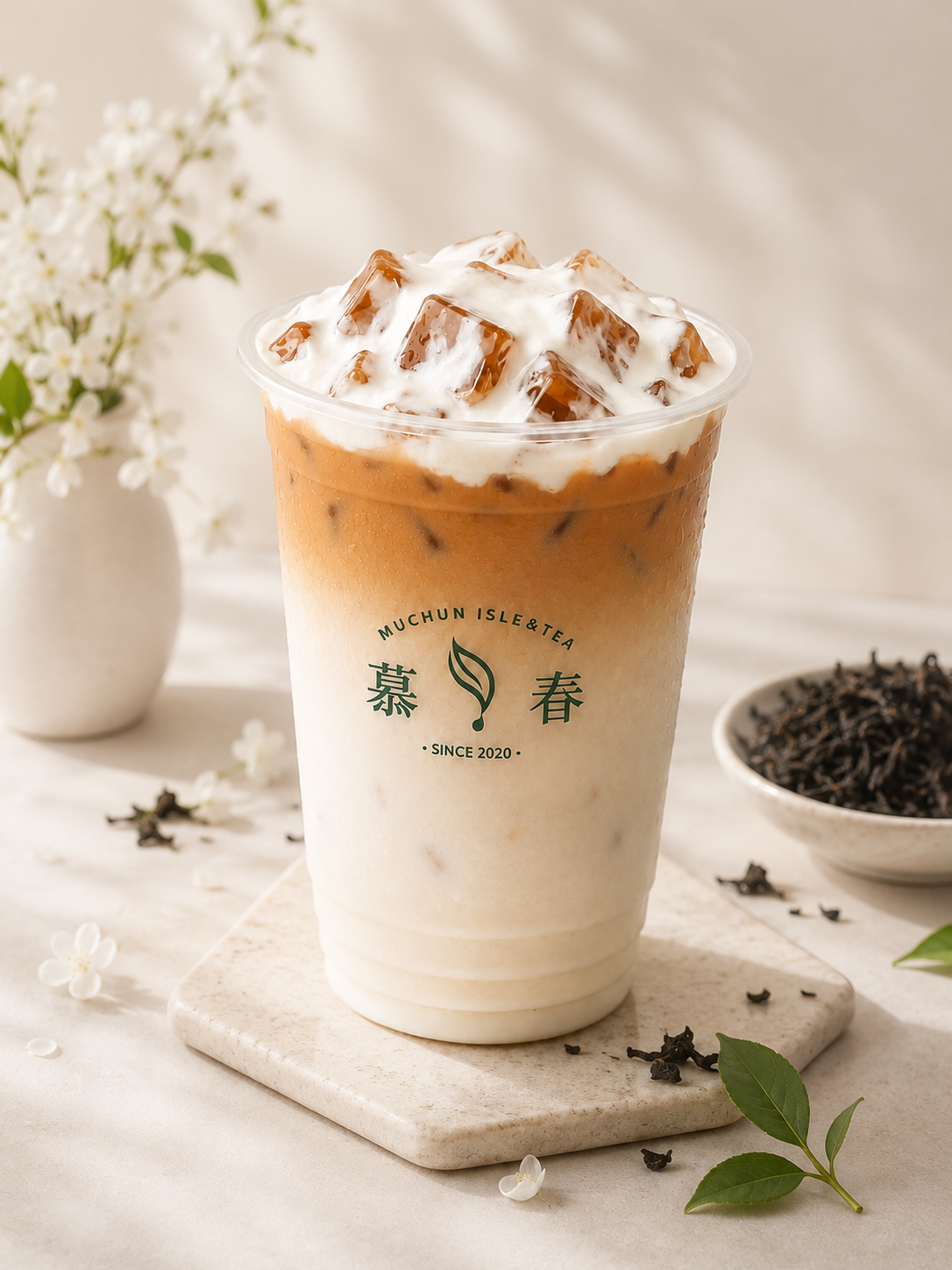 Two-tone layered black milk tea topped with thick cream and ice cubes beside loose tea leaves at Muchun Isle & Tea, a Taiwanese crafted Tea & Bubble Tea Shop in Bayside