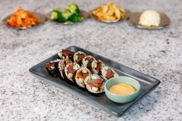 Plate of sliced gimbap rolls with dipping sauce and side dishes