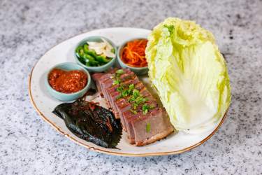 Pork belly slices with lettuce, paste, and vegetable garnishes on a plate