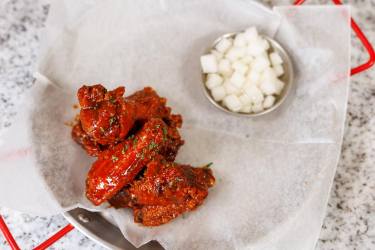 Saucy Korean fried chicken wings with pickled radish in a lined metal tray