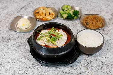 Spicy tofu stew in a black pot with rice and Korean side dishes