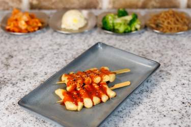 Two skewers of spicy rice cakes with sauce on a gray plate