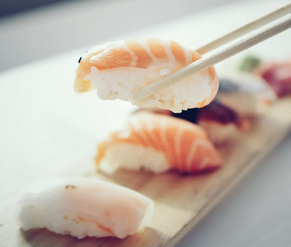 Chopsticks picking up a piece of salmon nigiri sushi, with the same - style sushi placed below