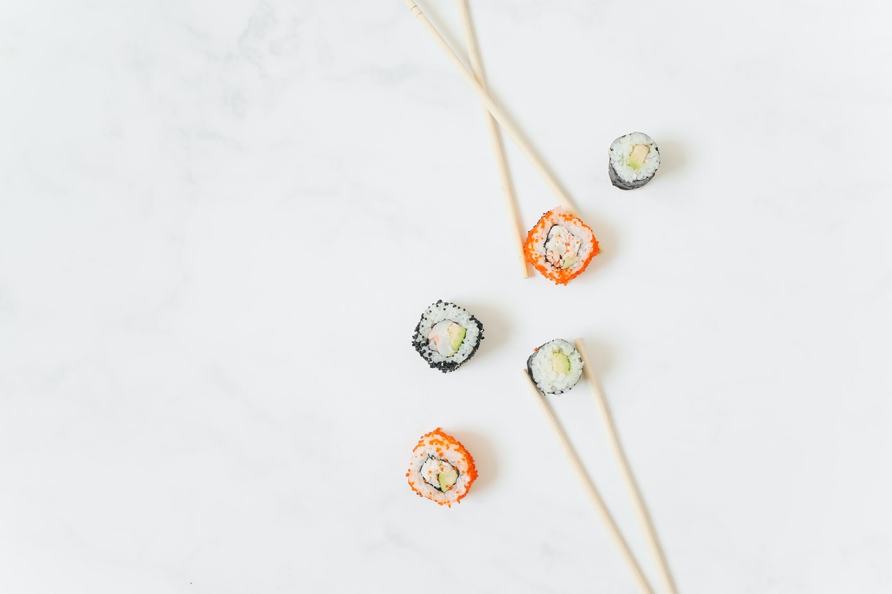 sushi 5Different types of mini sushi rolls placed on a white background, paired with chopsticks