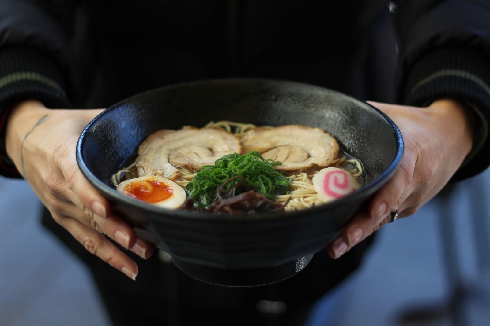 Hands holding a bowl of classic chashu ramen with seaweed and narutomaki at Ninja Ramen Restaurant in Lancaster