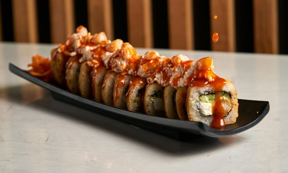 Tempura sushi roll with spicy sauce and seafood toppings on a black plate at Noodle House, a Japanese Sushi Restaurant in Flemington