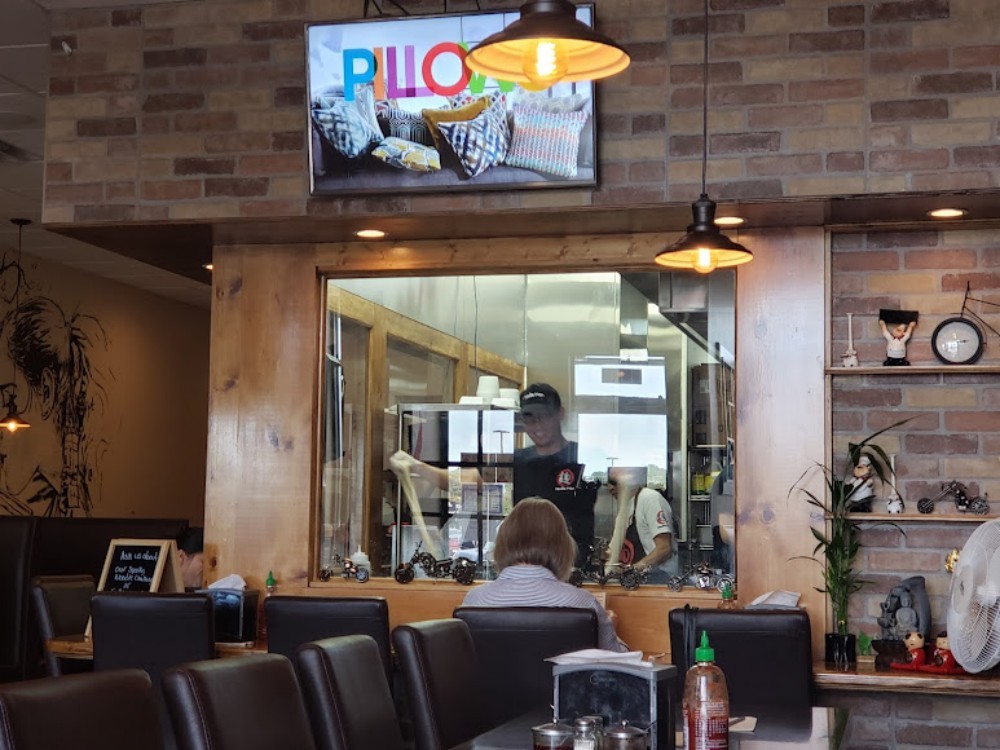 Dining area view with open kitchen and hanging lights at Noodle Man , a Noodle shop in Virginia Beach