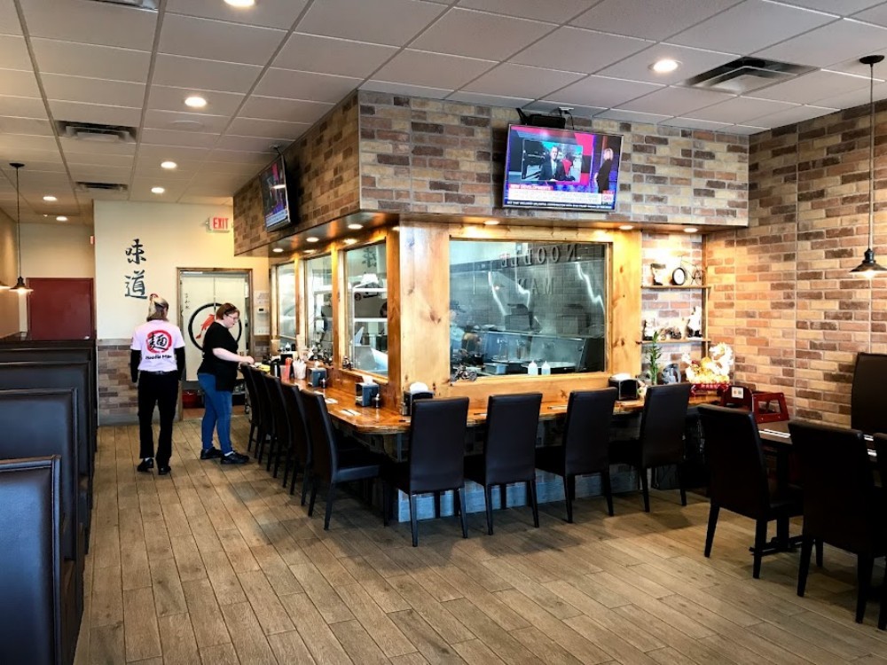Open kitchen area with staff and brick wall decor at Noodle Man , a Noodle shop in Virginia Beach