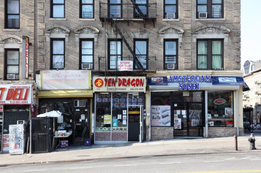 A street-level view of a brick building with storefronts for a Deli, Ten Dragon Chinese, and Amsterdam Sushi in NYC.