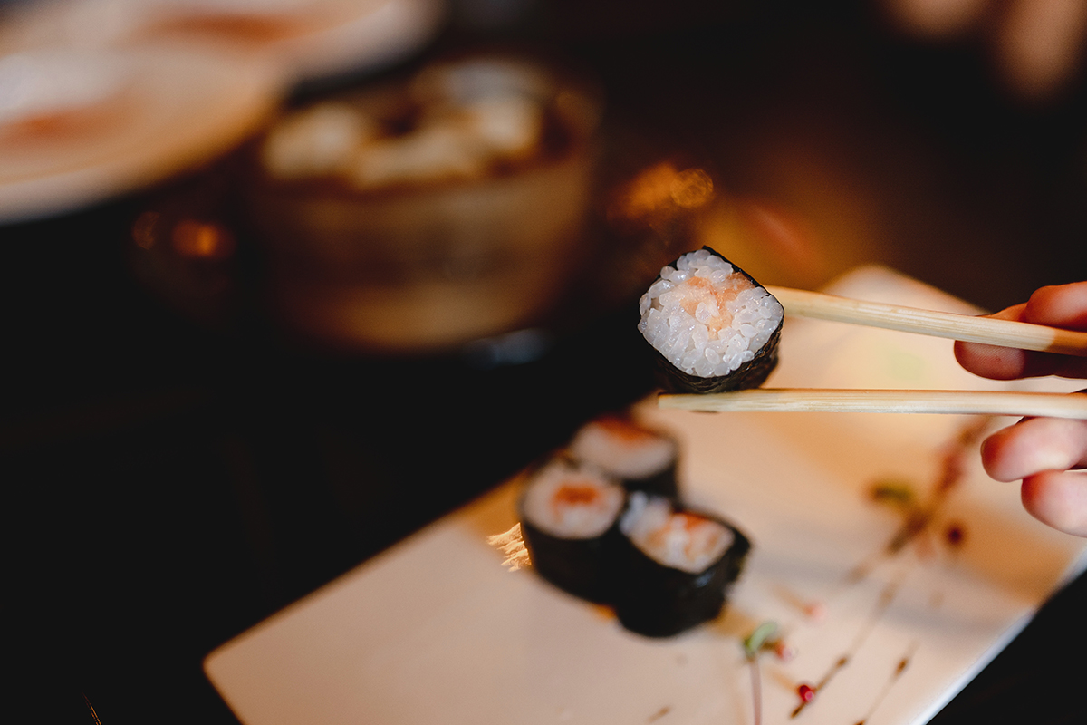 Small seaweed sushi roll held by wooden chopsticks at Oishii Express, a Japanese Restaurant in Oklahoma City