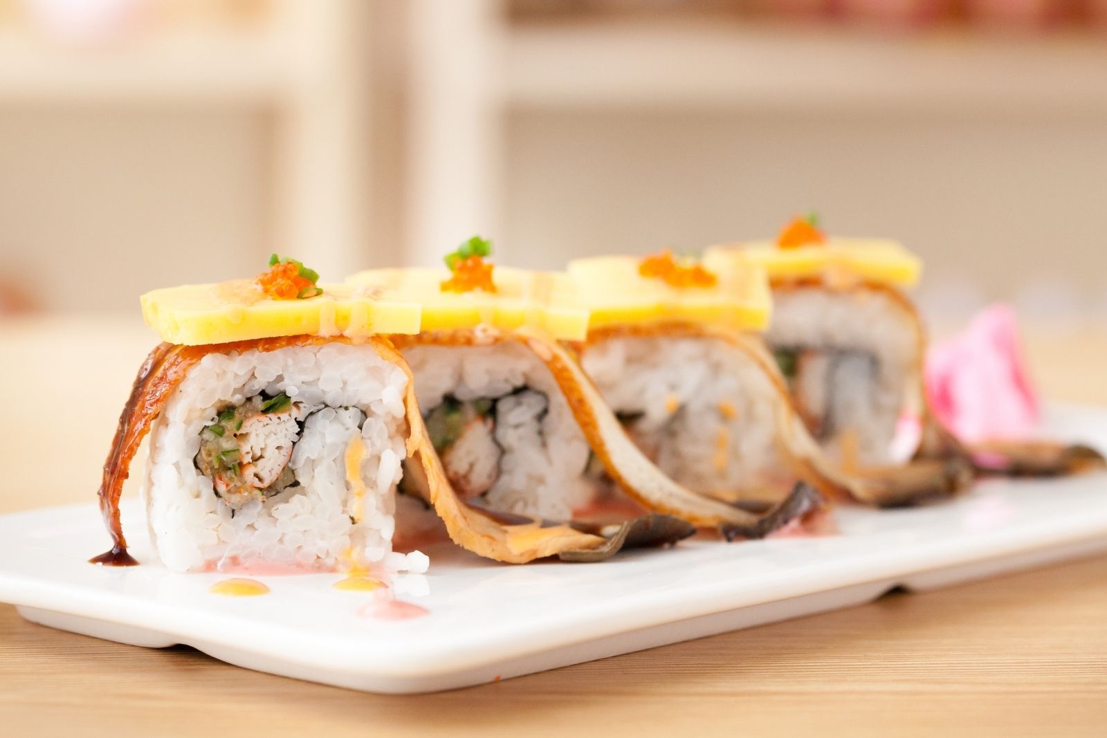 Grilled eel sushi rolls topped with mango and garnish on white plate