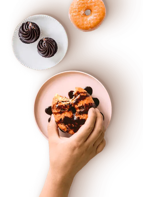 Hand holding bitten chocolate‑drizzled donut with cupcakes at OneZo，a Bubble Tea Store in Brookline