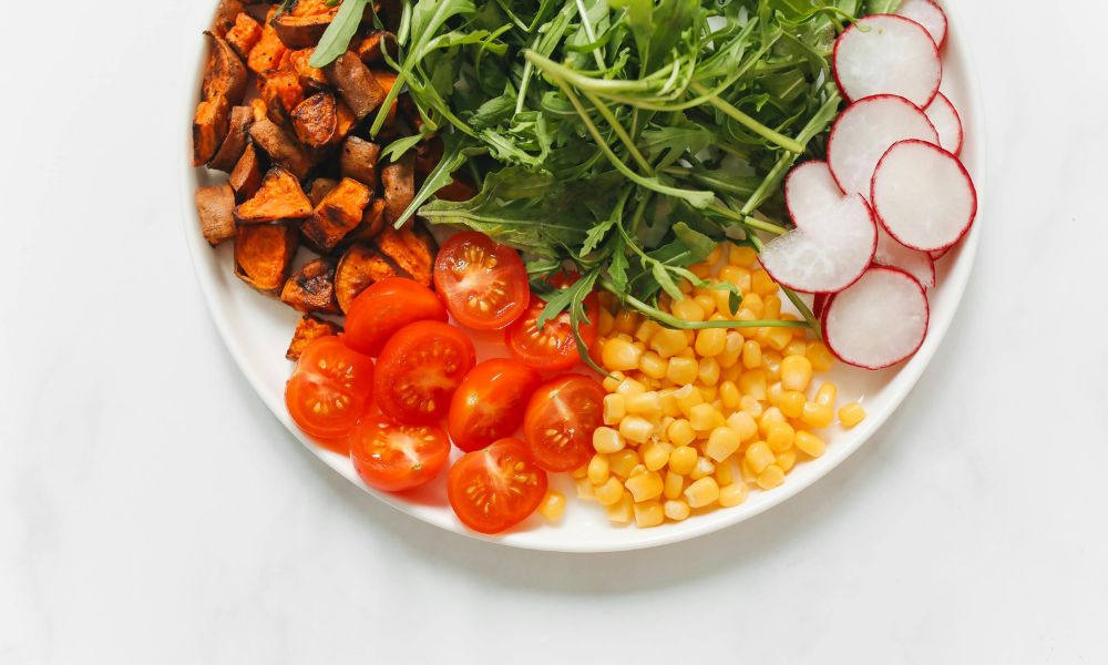 Overhead shot of colorful salad plate with arugula, sweet potato, corn, tomato and radish on clean white marble at Zen Bowl, a Healthy Poke Restaurant in Imperial