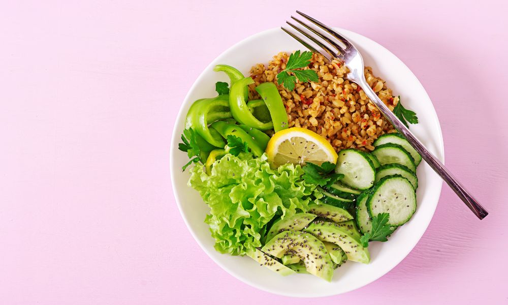 Top-down bright white salad bowl with bulgur grain, avocado, cucumber, bell pepper and lemon on pastel pink backdrop at Zen Bowl, a Healthy Poke Restaurant in Imperial