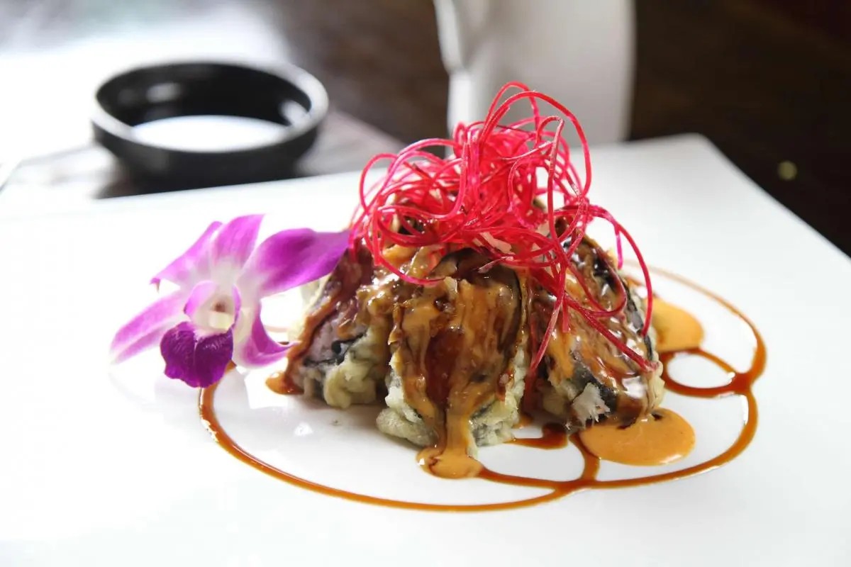 Sushi roll with drizzled sauces and red garnish, paired with orchid, at Oriental Palace, a Asian Restaurant in Lawnside