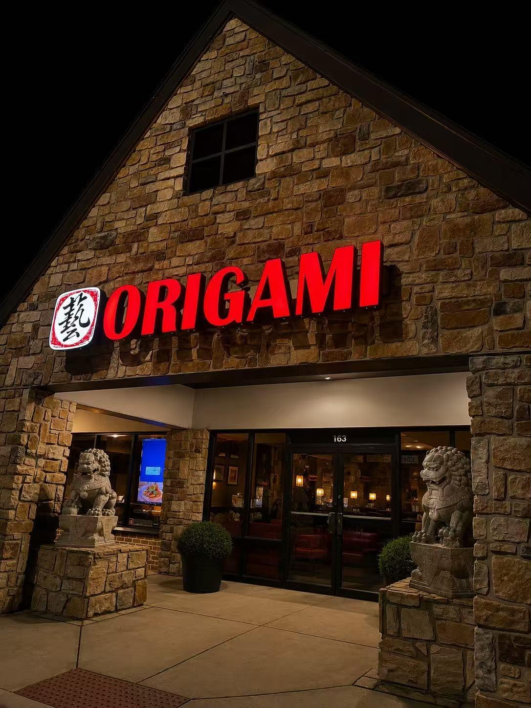Night exterior stone building with red ORIGAMI sign and stone lion guardian statues at Origami Asian Fusion Exton, an Asian Fusion Restaurant in Exton