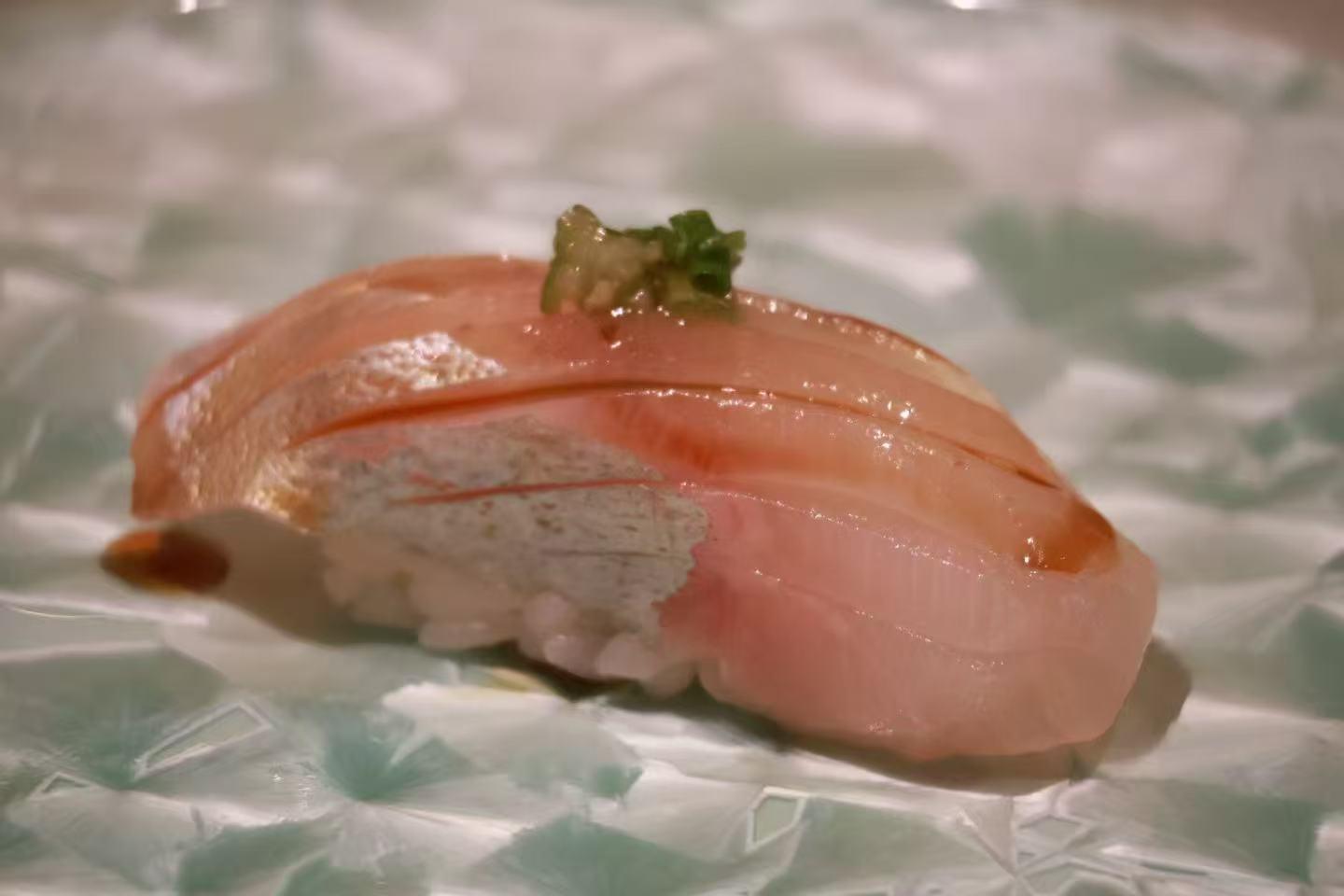Single piece of white fish nigiri sushi topped with fresh green garnish on patterned ceramic plate at Oroshi Sushi Omakase , a Japanese Restaurant in Philadelphia