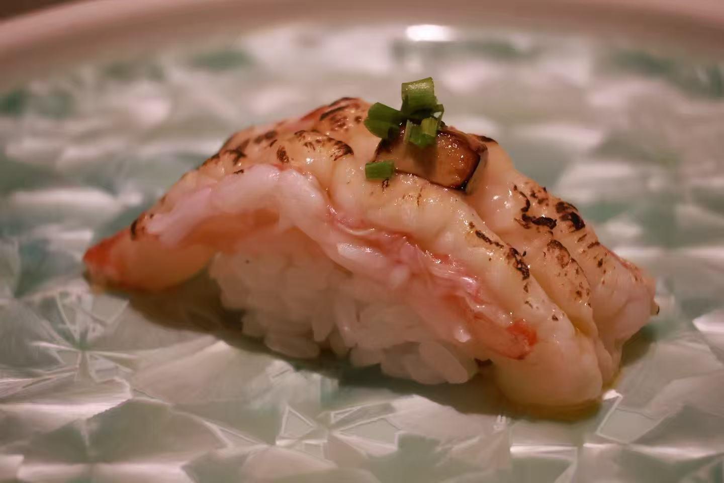 Torched shrimp nigiri sushi garnished with chopped green onion on light patterned ceramic plate at Oroshi Sushi Omakase , a Japanese Restaurant in Philadelphia