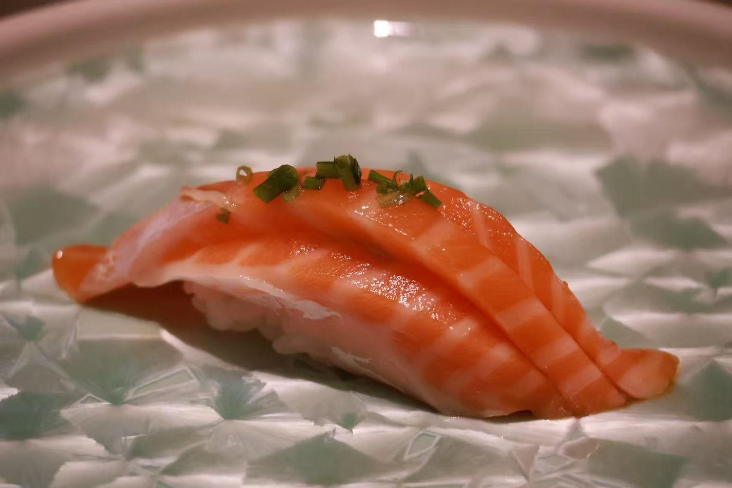 Glossy salmon nigiri sushi topped with finely sliced green onion on decorative ceramic plate at Oroshi Sushi Omakase , a Japanese Restaurant in Philadelphia